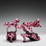 A pair of pink satin high-heeled sandals with black polka dots and large matching bow straps, shown from the back on a dark-to-light gray gradient studio background.