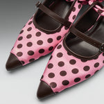 Pink satin Mary Jane shoes with dark brown polka dots, dark brown leather pointed toes, and matching dark brown straps, shown on a neutral gray background.