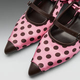 Pink satin Mary Jane shoes with dark brown polka dots, dark brown leather pointed toes, and matching dark brown straps, shown on a neutral gray background.