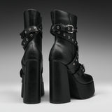 A pair of black platform ankle boots with chunky block heels, double platform soles, and multiple decorative straps with silver-tone grommets and buckles, shown from the back and side against a dark gray gradient background.