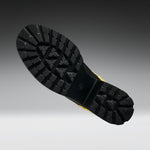 A close-up of a black rubber boot sole with deep tread patterns, shown against a dark gray to light gray gradient background.
