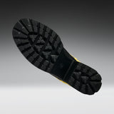 A close-up of a black rubber boot sole with deep tread patterns, shown against a dark gray to light gray gradient background.