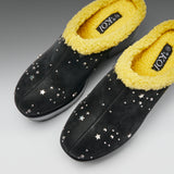 A pair of black slip-on mule-style slippers with bright yellow sherpa lining and scattered silver star-shaped studs, shown on a neutral gray background.