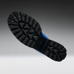 A close-up of a black rubber boot sole with deep tread patterns, shown against a dark gray to light gray gradient background.
