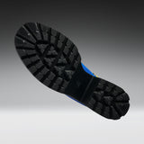 A close-up of a black rubber boot sole with deep tread patterns, shown against a dark gray to light gray gradient background.