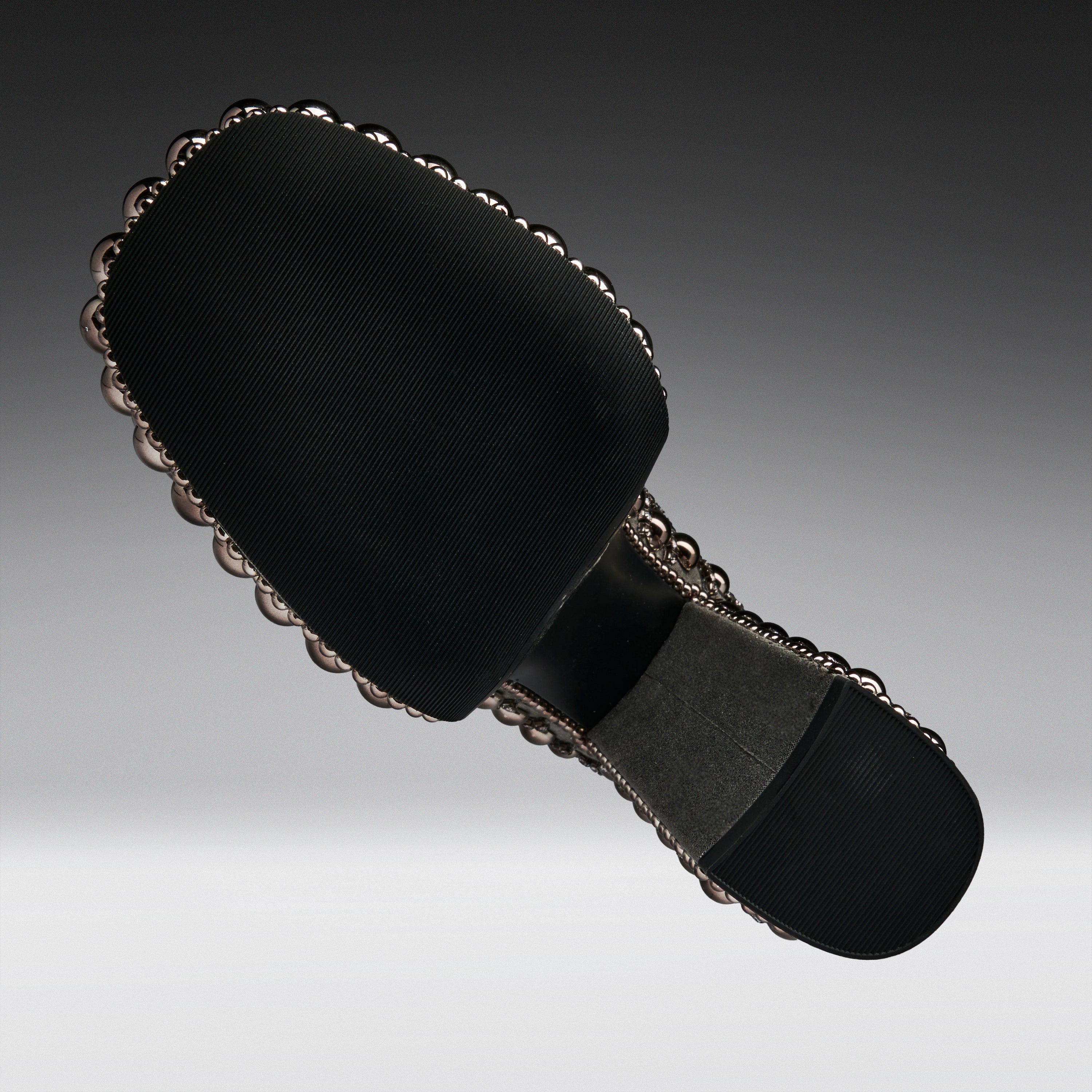 A black fabric-covered shoe sole with a decorative scalloped metallic edge and a gray footbed, shown on a gradient gray background.