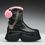 A black leather ankle boot with a chunky lug sole, decorated with a fluffy pink faux-fur trim, a pink pom-pom, and a silver chain with a butterfly charm.