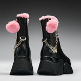 A pair of black ankle boots with fluffy pink faux-fur trim, pink pom-poms, and silver chain details, shown from the back on a gray gradient background.