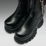 A pair of black leather ankle boots with chunky lug soles and a silver chain detail, shown on a neutral gray background.