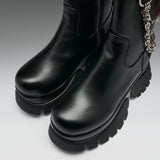 A pair of black leather ankle boots with chunky lug soles and a silver chain detail, shown on a neutral gray background.