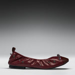 A single burgundy leather ballet flat with star-shaped metallic embellishments and a dark brown pointed toe, shown in profile against a gray gradient studio background.