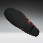A single shoe shown from a high-angle back view, displaying a black textured outsole and a dark burgundy-red inner lining against a gray gradient background.