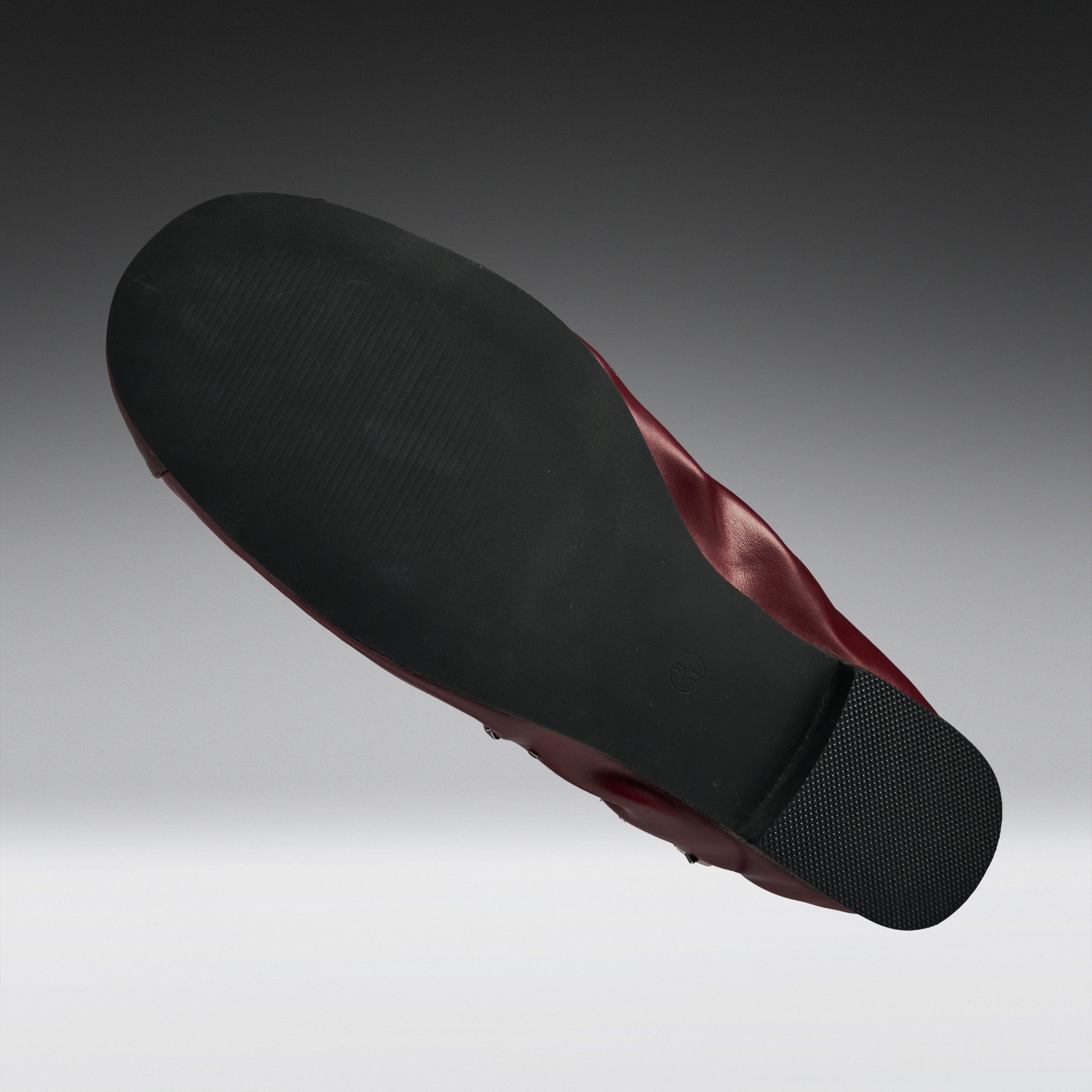 A single shoe shown from a high-angle back view, displaying a black textured outsole and a dark burgundy-red inner lining against a gray gradient background.