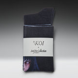 A pair of dark charcoal gray crew socks folded and wrapped in a white paper band. The band features the text 'KOI x Junji Tko Collection' and a printed illustration of a character from the anime Junji No Naka de Amu.