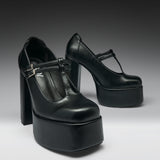 A pair of black leather high-heeled platform Mary Jane shoes with T-strap buckles, photographed on a dark-to-light gray gradient studio background.
