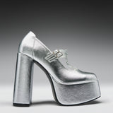 A metallic silver platform high-heeled shoe with a Mary Jane strap and double buckle detail, shown from a side profile on a dark-to-light gray gradient background.