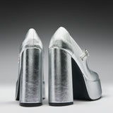 A pair of metallic silver high-heeled pumps with block heels and platform soles, shown from the back on a dark-to-light gray gradient studio background.