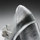 Close-up of a metallic silver leather shoe with a pointed toe and double strap detailing on a dark gray gradient background.