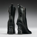 A pair of black leather ankle boots with chunky, wavy transparent block heels, shown from the back on a dark gray gradient background.