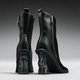 A pair of black leather ankle boots with chunky, wavy transparent block heels, shown from the back on a dark gray gradient background.