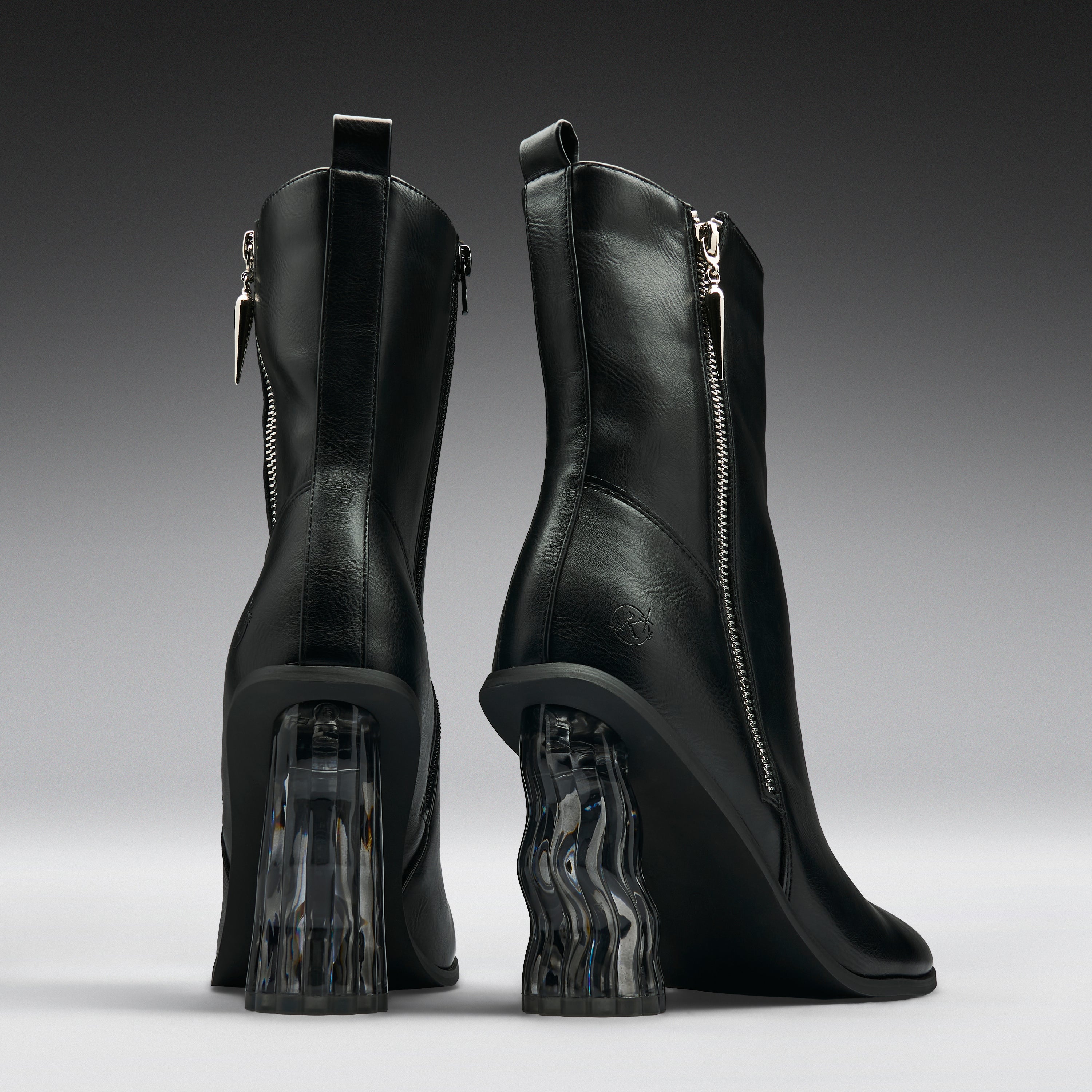 A pair of black leather ankle boots with chunky, wavy transparent block heels, shown from the back on a dark gray gradient background.