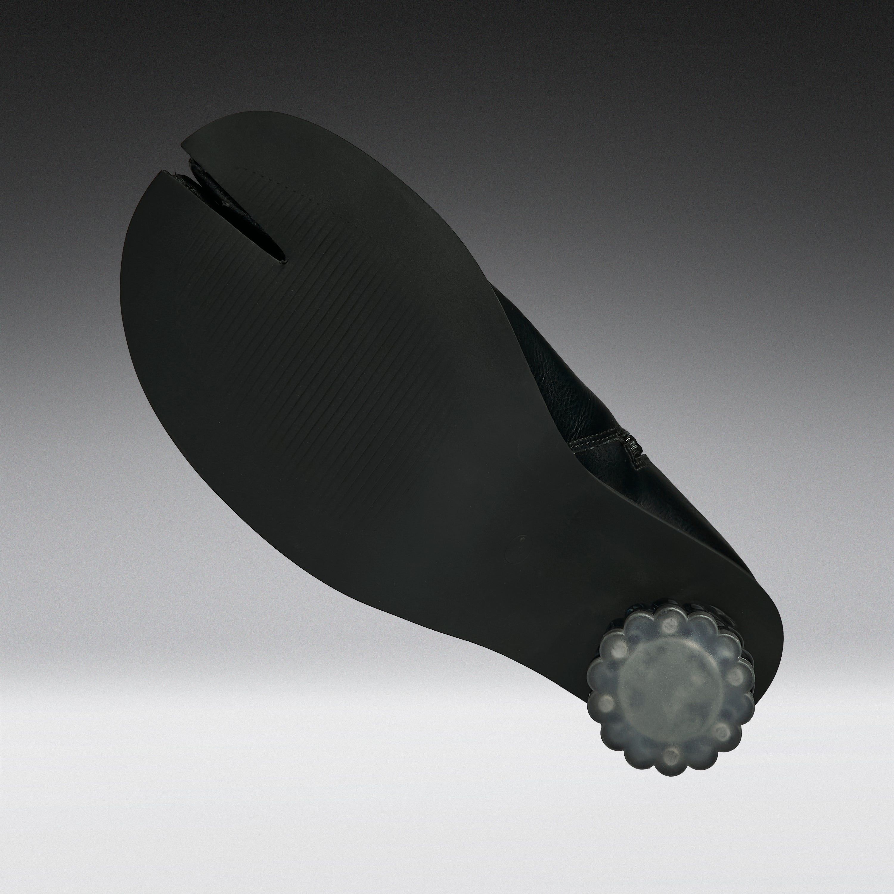A black split-toe shoe sole with a textured surface and a translucent gray decorative end cap, shown on a dark-to-light gray gradient background.