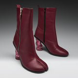 A pair of dark burgundy leather ankle boots with a split toe, side zippers, and chunky translucent pink block heels, shown on a gray gradient studio background.