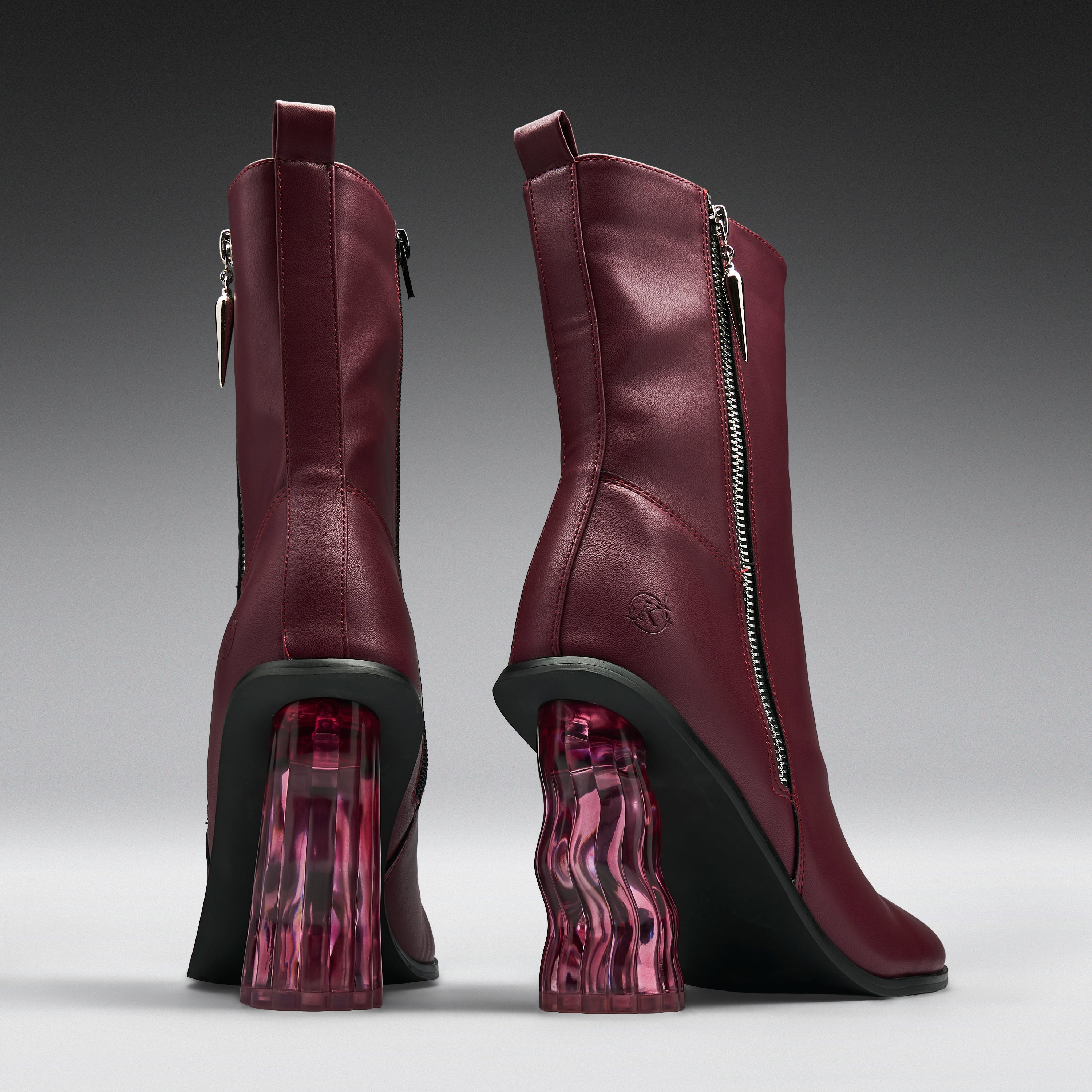 A pair of burgundy leather ankle boots with chunky black and translucent pink wavy block heels, shown from the back and side on a gray gradient background.