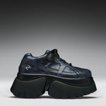 A single dark navy blue leather sneaker with a chunky black platform sole, photographed from a side profile against a gray gradient studio background.