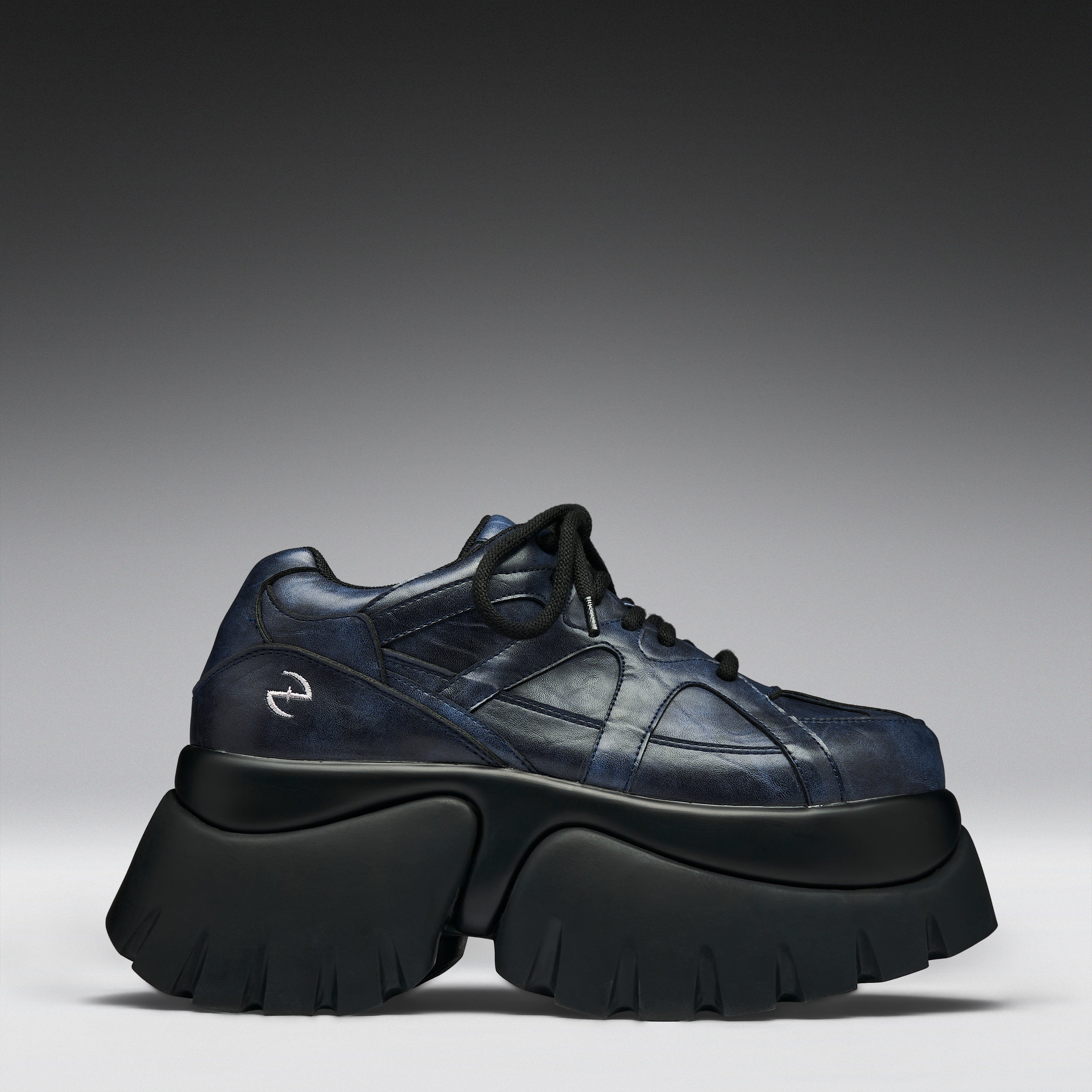 A single dark navy blue leather sneaker with a chunky black platform sole, photographed from a side profile against a gray gradient studio background.