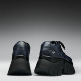 A pair of dark navy blue leather high-top sneakers with chunky black platform soles, shown from the rear three-quarter view against a dark gray gradient studio background.