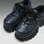 A pair of dark navy blue leather platform sneakers with chunky black soles and black laces, photographed on a neutral gray studio background.