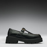 A single black leather Mary Jane loafer with a chunky lug sole, a gold buckle strap, and decorative gold stitching on the toe, shown against a dark gray gradient background.