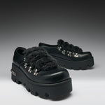 A pair of black leather platform mule shoes with fluffy black faux-fur trim and silver-tone decorative studs, shown on a dark-to-light gray studio background.