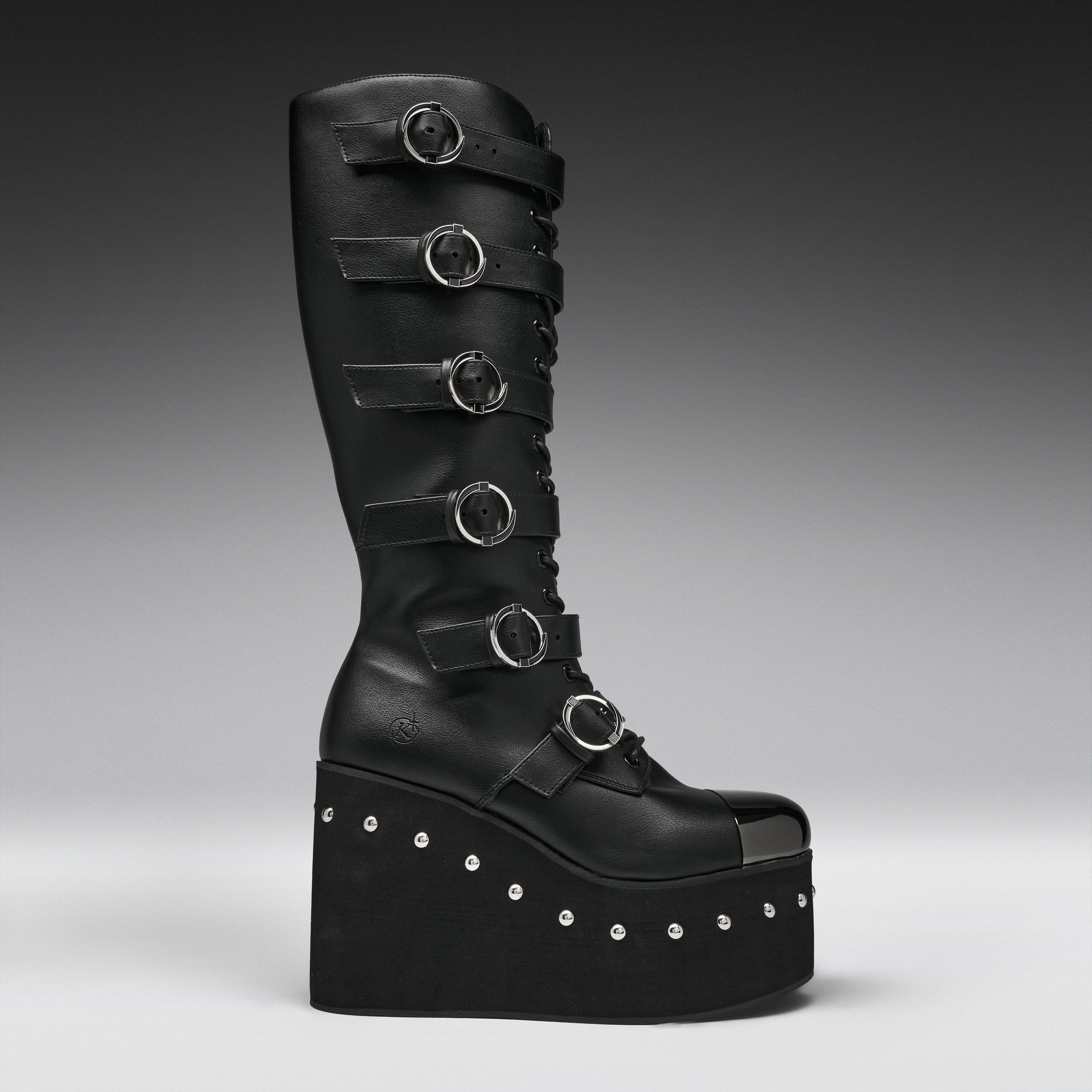 A tall black leather platform boot with multiple horizontal strap details and silver-tone circular buckles, photographed against a dark gray gradient studio background.