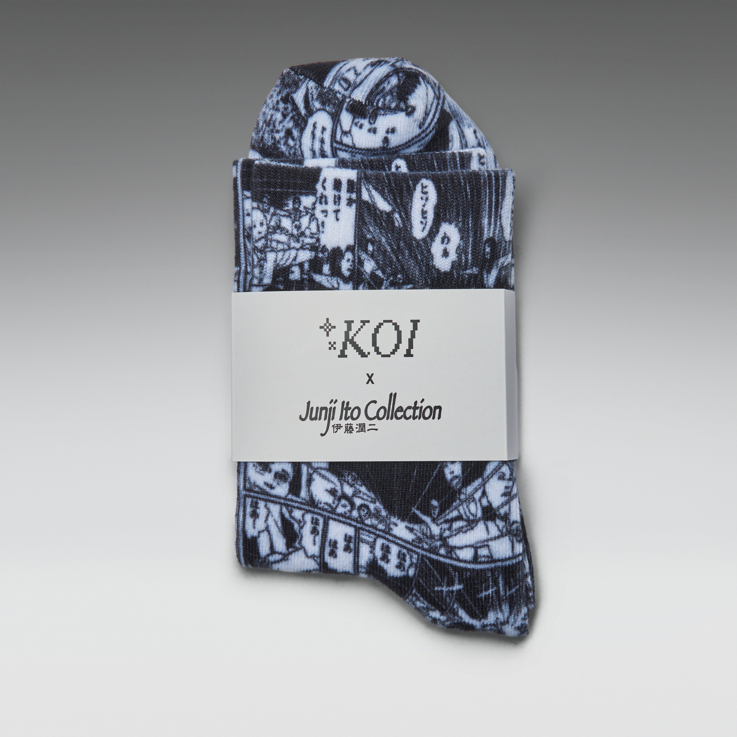 A folded pair of patterned socks or hosiery with a dark navy and white illustrated print, wrapped in a white paper band labeled 'KOI x Junji Itto Collection' on a gray gradient background.