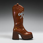 A brown leather cowboy-style boot with a chunky wooden block heel, decorated with embroidered stars, lightning bolts, and a bow on the shaft, shown against a dark gray gradient background.