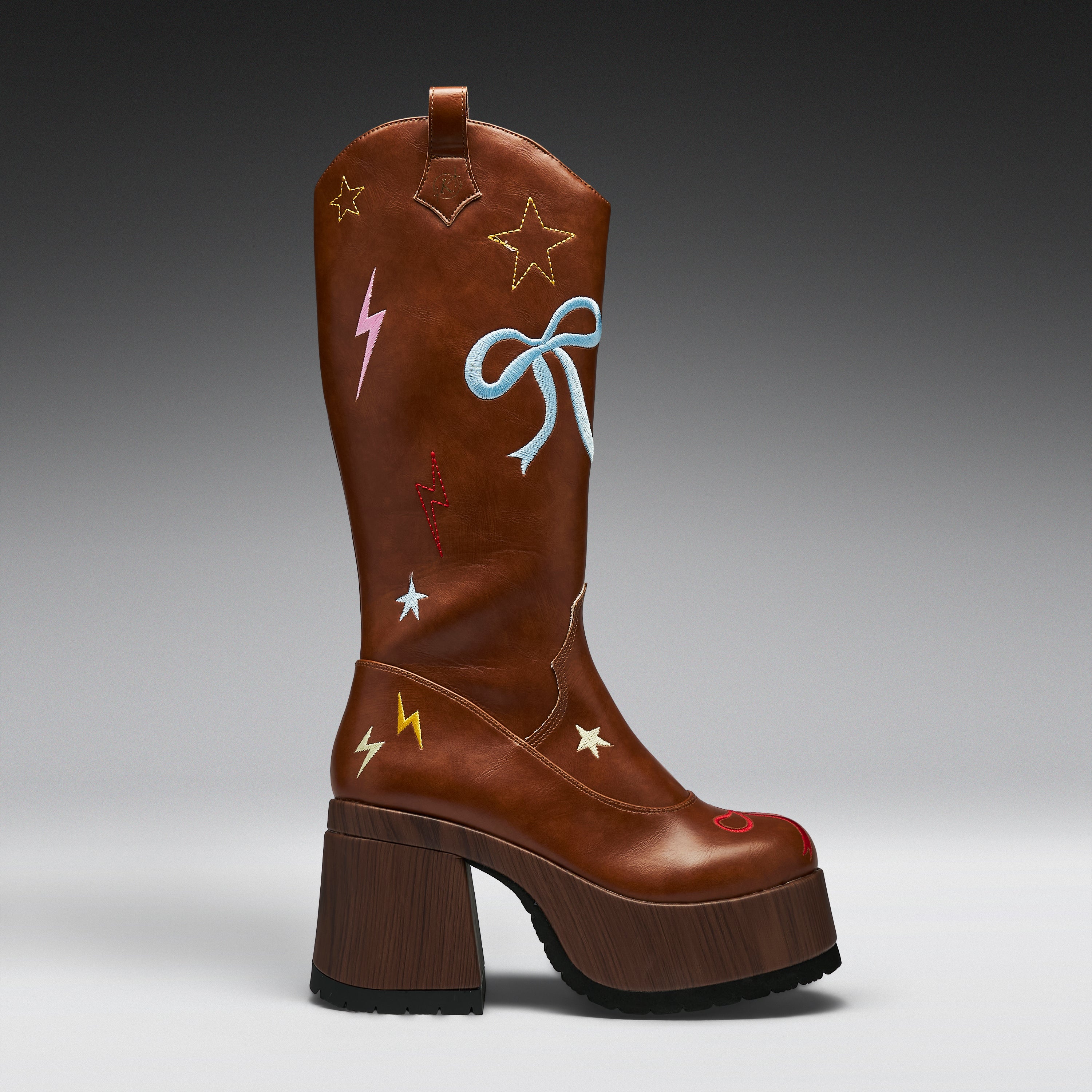 A brown leather cowboy-style boot with a chunky wooden block heel, decorated with embroidered stars, lightning bolts, and a bow on the shaft, shown against a dark gray gradient background.