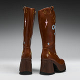 A pair of tall brown leather boots shown from the back, featuring colorful embroidered stars, lightning bolts, and swirls on the shaft, with chunky dark brown platform heels and black soles.