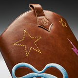 Close-up of a brown leather bag featuring embroidered star motifs in yellow, a blue bow design at the bottom, and a small pink lightning bolt detail on a dark gradient background.
