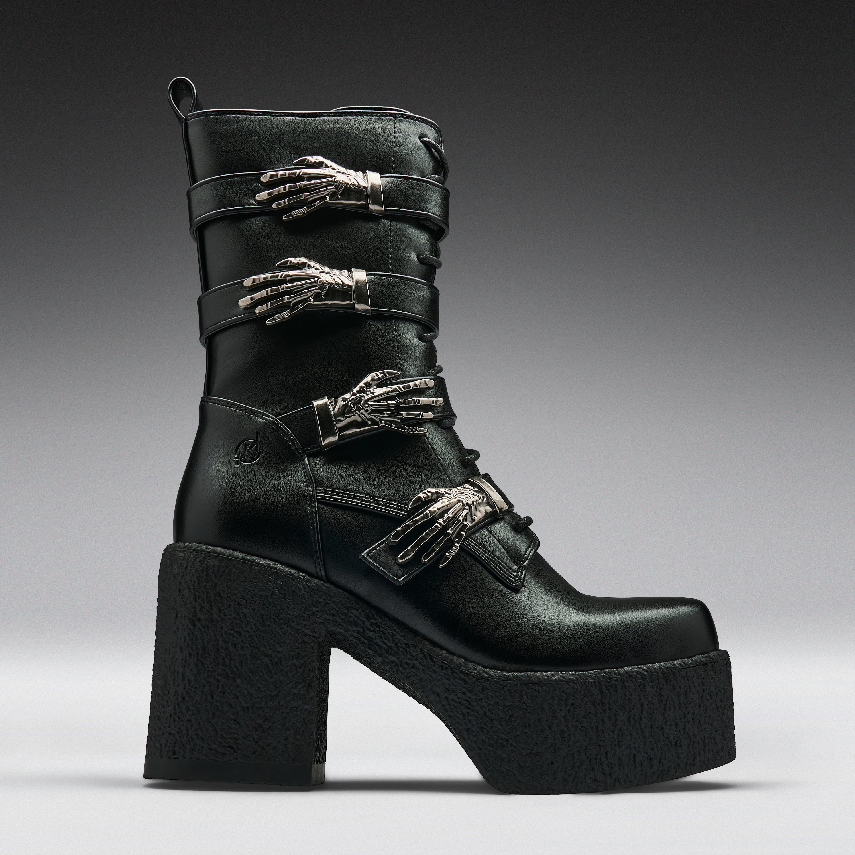 A black leather ankle boot with a chunky platform sole and high block heel, decorated with three silver metallic skeleton hand embellishments on the straps, shown against a dark gray gradient background.