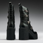 A pair of black leather ankle boots with chunky platform soles and high block heels, decorated with silver skeleton hand and chain buckle embellishments, shown from the back and side against a dark gray gradient background.