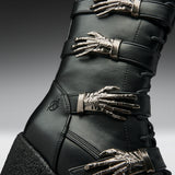 Close-up of a black leather boot with multiple metallic skeleton hand embellishments and silver-toned buckles, shown against a dark gray gradient background.