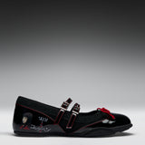 A black Mary Jane-style shoe with double straps, red contrast stitching, a red bow detail, and graphic character artwork on the side, photographed on a gray gradient studio background.