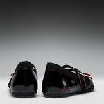 A pair of black patent leather Mary Jane shoes with black fleece lining, red contrast stitching, and character graphics on the sides, shown from the back against a gradient gray background.