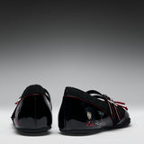 A pair of black patent leather Mary Jane shoes with black fleece lining, red contrast stitching, and character graphics on the sides, shown from the back against a gradient gray background.