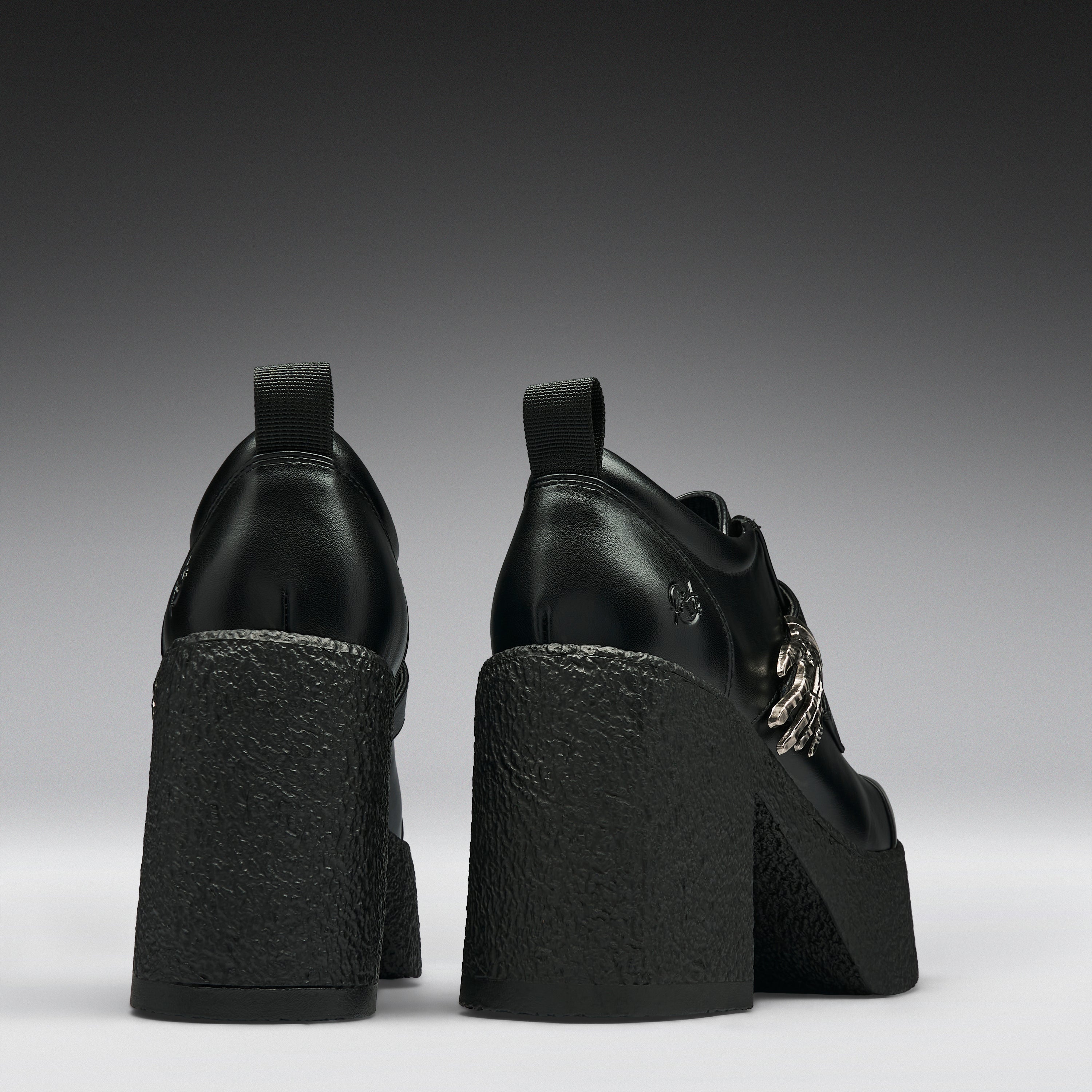 Black leather platform ankle boots with chunky textured block heels and silver chain details, shown from the back on a dark gray gradient background.