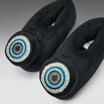 A pair of black plush slippers with circular embroidered eye motifs on the toes, featuring blue, white, and black details, set against a neutral gray background.
