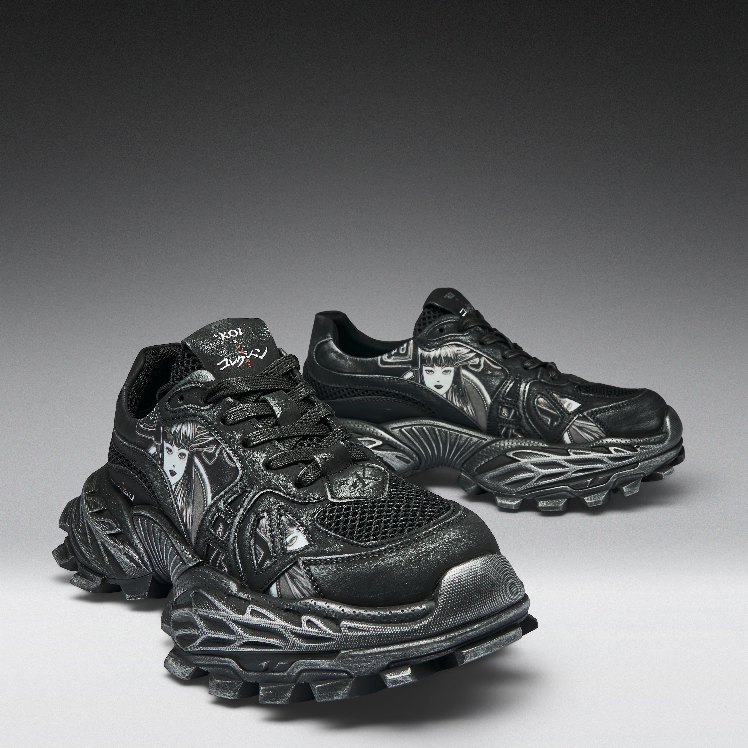 A pair of black and dark gray chunky athletic sneakers with sculpted, textured soles and metallic silver graphic details, displayed on a dark-to-light gray gradient studio background.