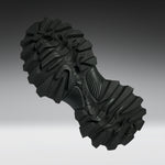 A single black rugged outsole or shoe tread shown floating against a smooth gray gradient background.